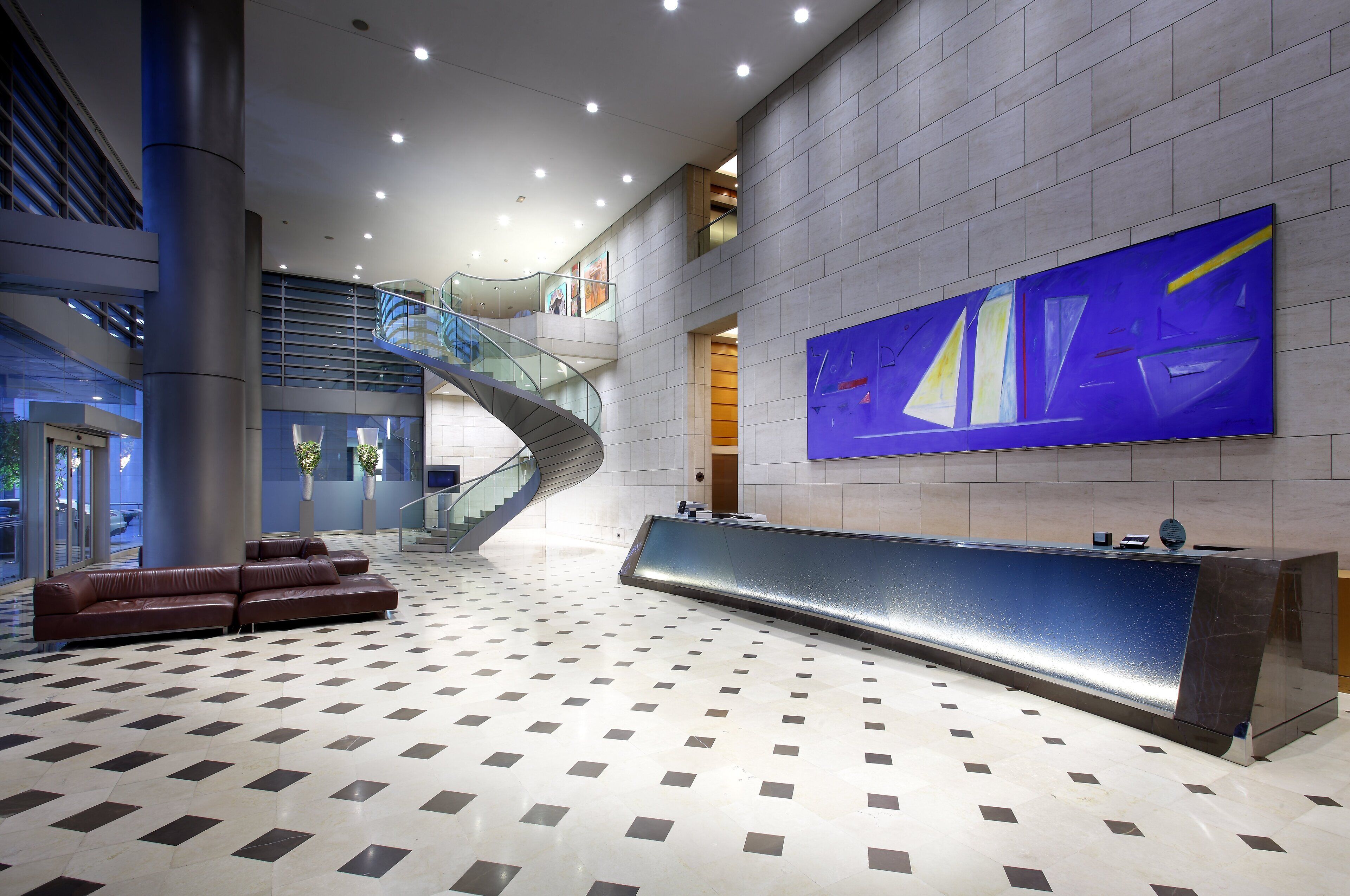 Eine moderne Lobby mit einer geschwungenen Rezeption, einer Treppe und einem großen abstrakten Gemälde an der Wand.