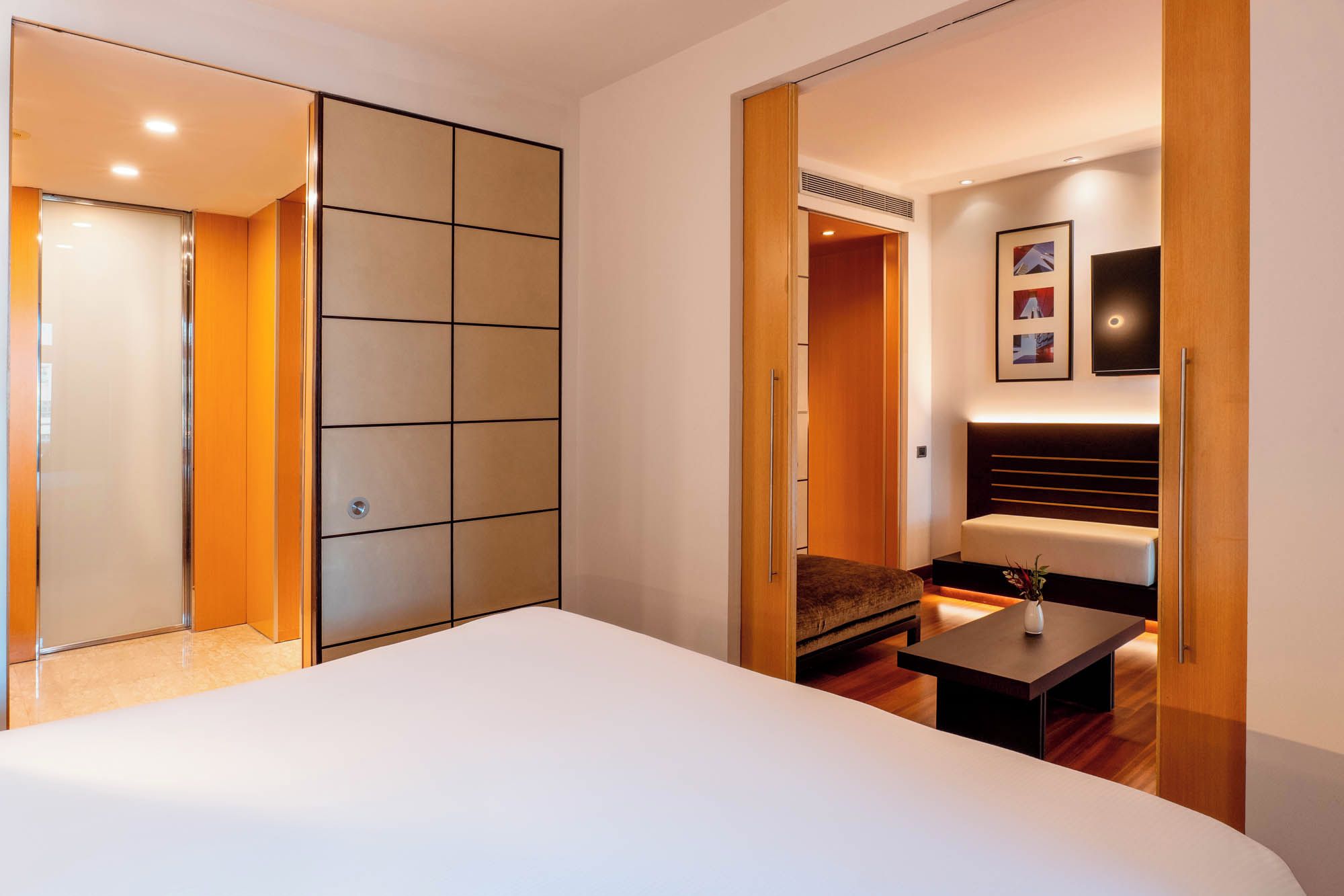 A hotel room with a large bed, a seating area with a table, and a wardrobe with sliding doors.