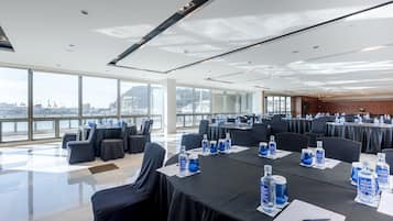 A conference room with tables set for a meeting, large windows offering a view of the city, and a modern ceiling design.