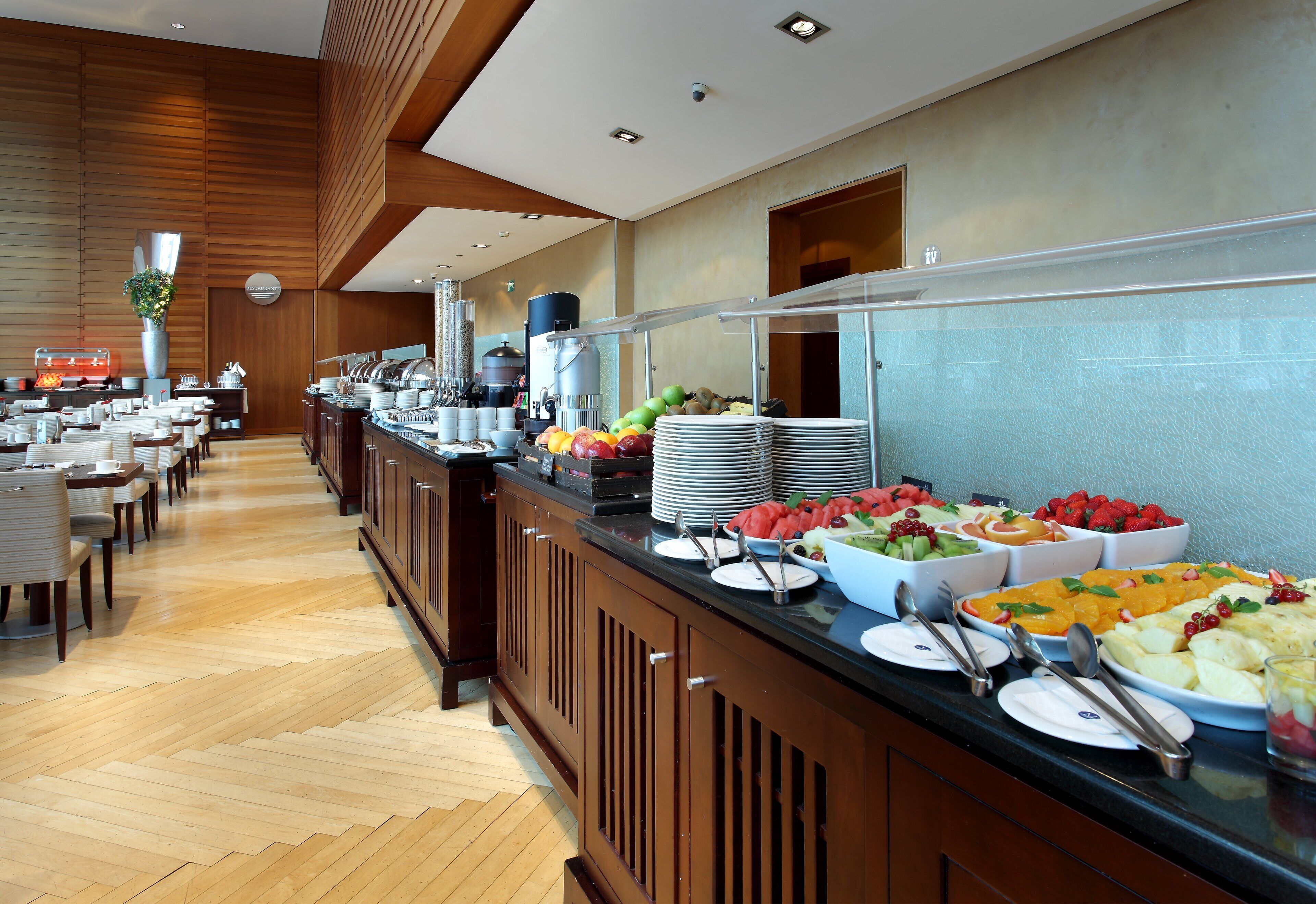 Uma área de buffet com vários pontos de serviço de comida, painéis de madeira e um balcão longo com diversos pratos.