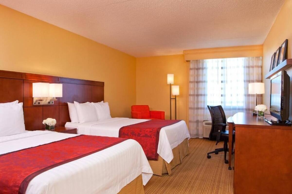 Ein Hotelzimmer mit zwei Betten, einem Schreibtisch, einem Sessel und einem Fernseher.