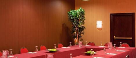 Une salle de conférence avec des tables disposées pour une réunion, une plante en pot et une porte.