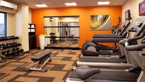 Une salle de sport équipée de tapis de course, d’haltères et d’un miroir.