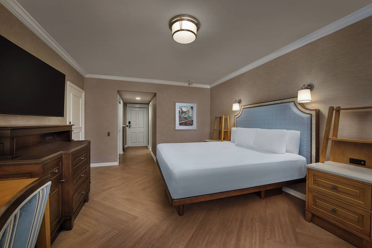 Ein Hotelzimmer mit einem großen Bett, einem hölzernen Schminktisch, Nachttischen, einem Flachbildfernseher und einer Deckenleuchte.