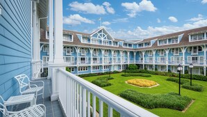 Un hotel con fachada azul, barandillas blancas y un jardín bien cuidado con un macizo de flores central.
