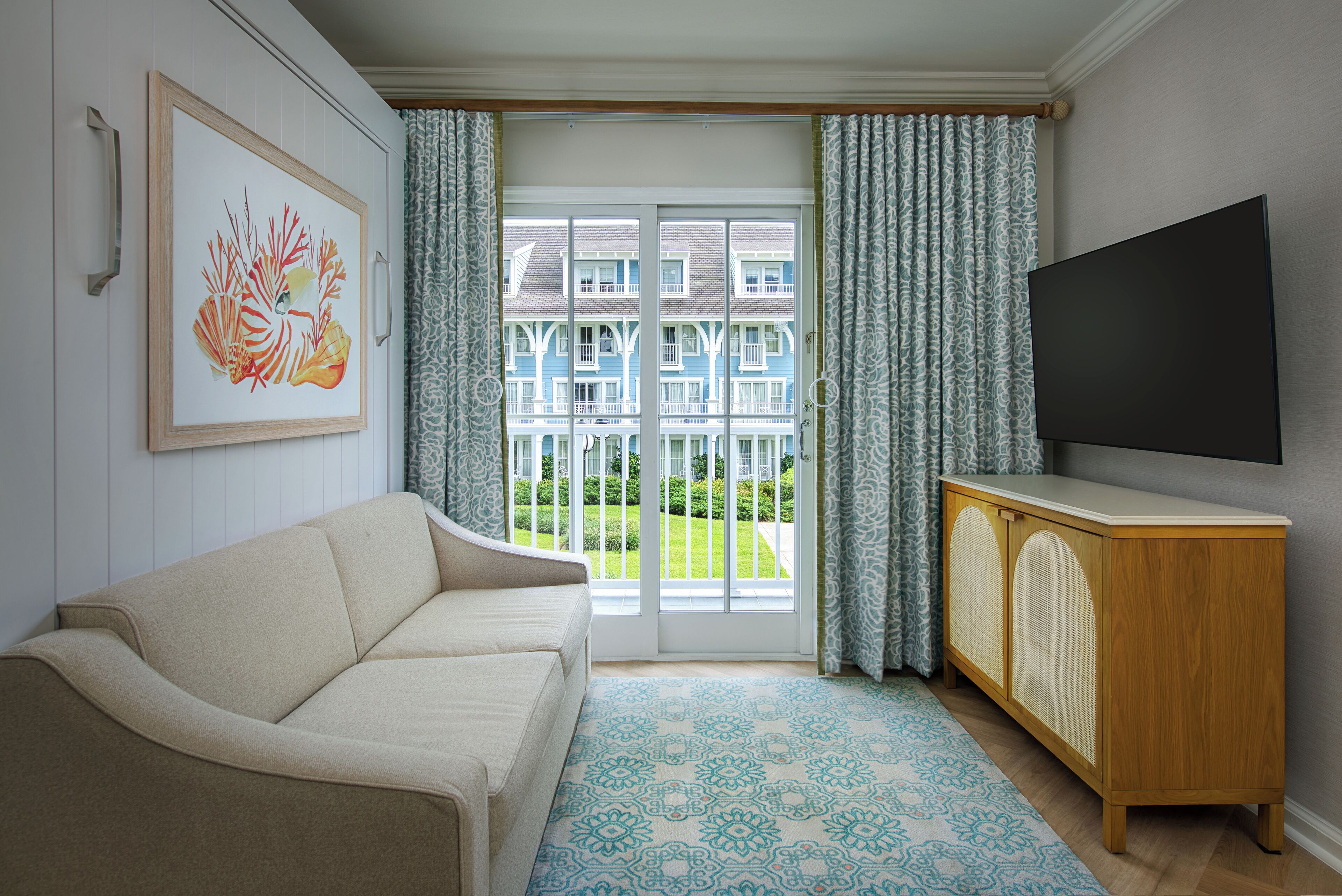 A living room with a beige sofa, a TV on a wooden cabinet, and a patterned rug.