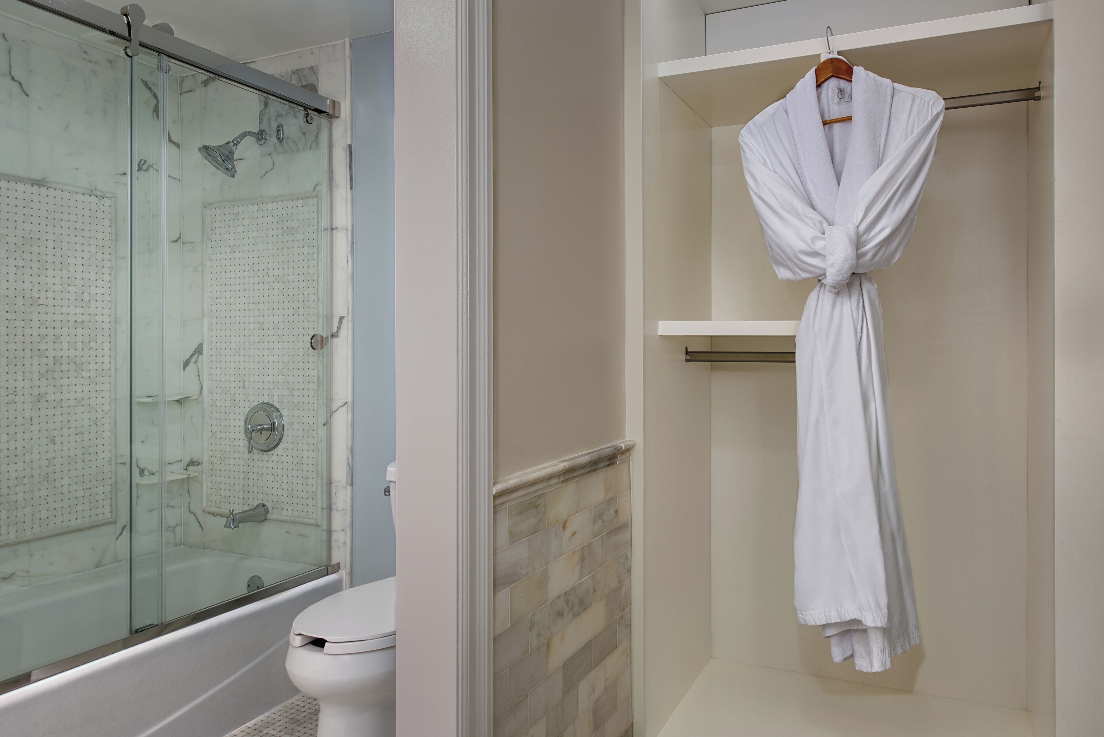 A bathroom with a glass-enclosed shower, a white toilet, and a robe hanging on a rack.