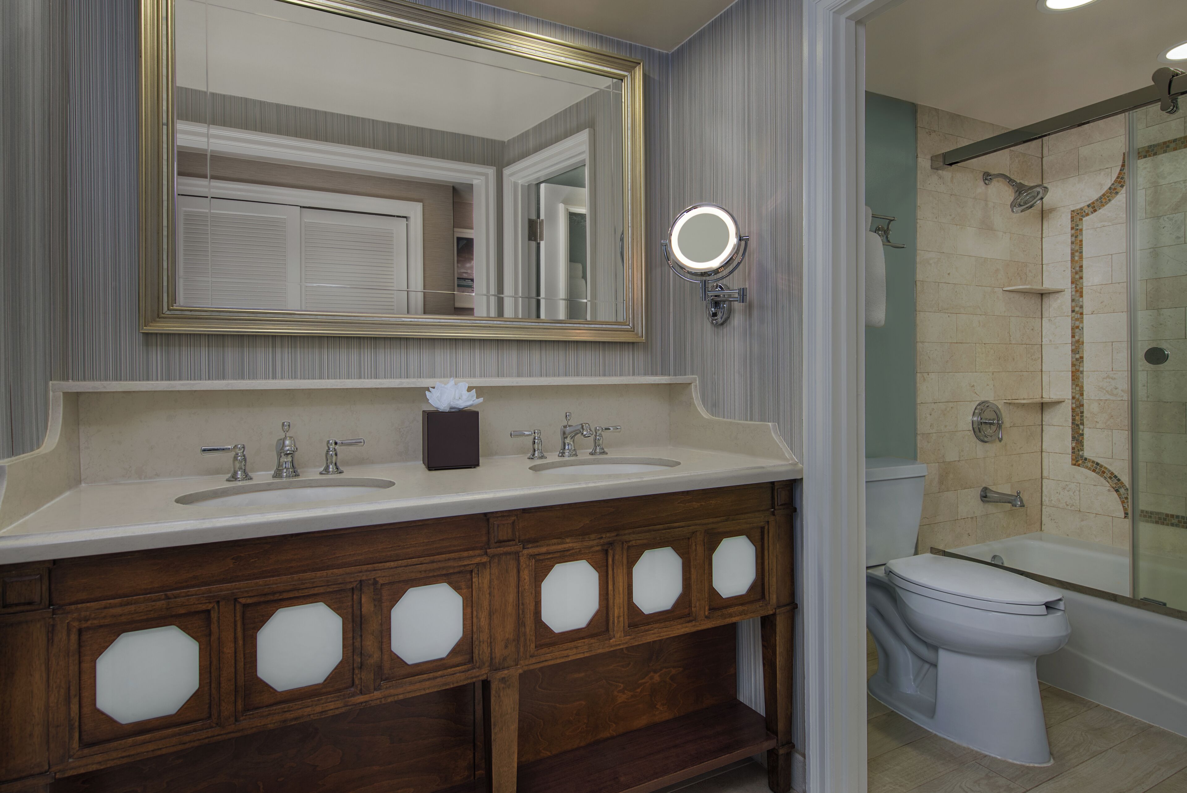A bathroom with a double sink vanity, a mirror, a round light, and a shower area.