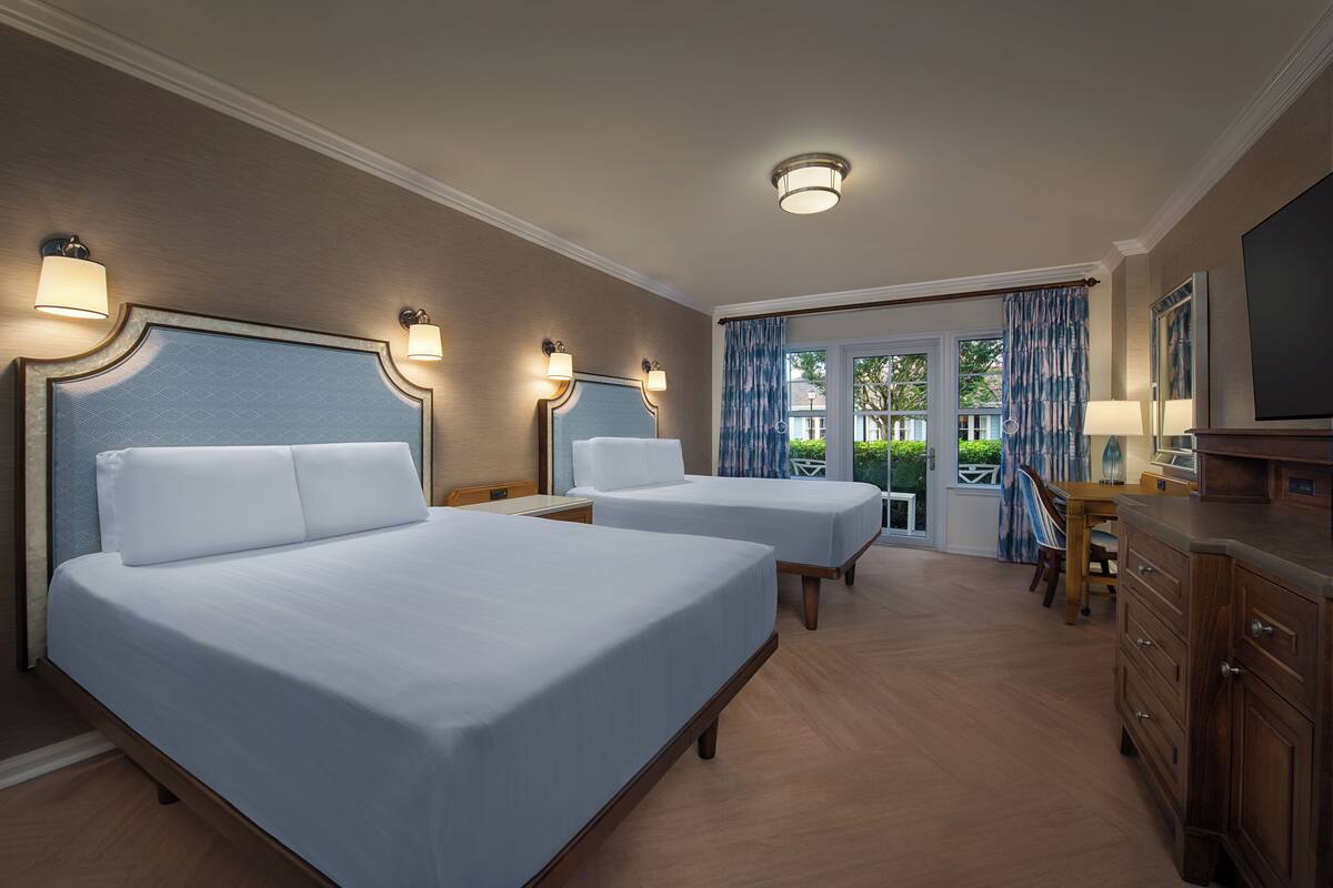 Ein Hotelzimmer mit zwei Betten, einem Holzschrank, einem Fernseher und Blick ins Freie durch ein großes Fenster.