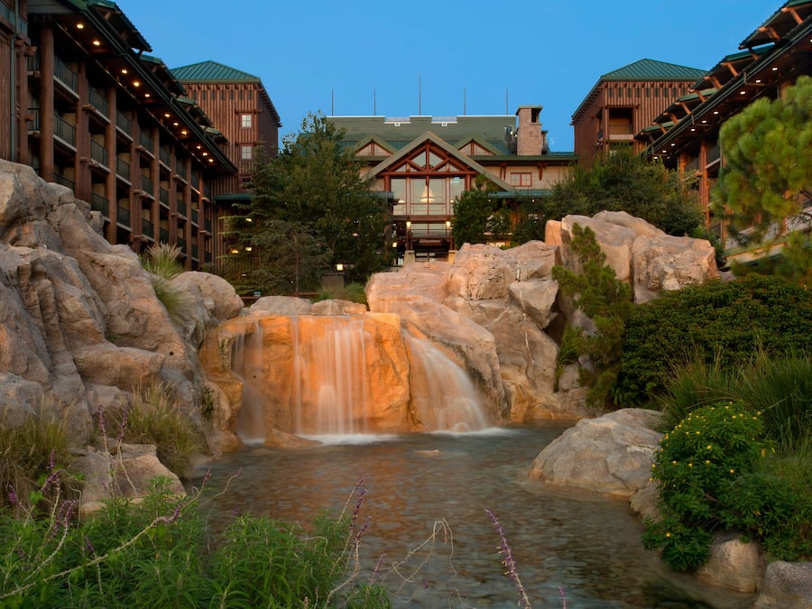 Un hotel con una cascada, rocas grandes y abundante vegetación.