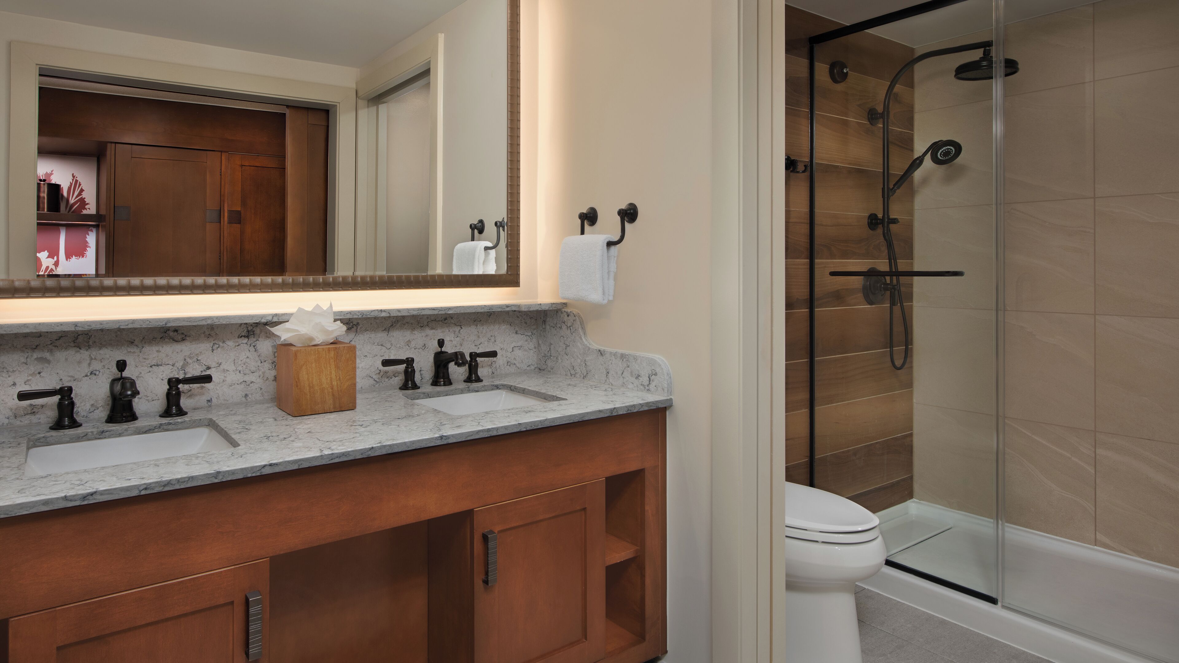 A bathroom with a marble countertop, wooden vanity, a mirror, a toilet, and a glass-enclosed shower area.