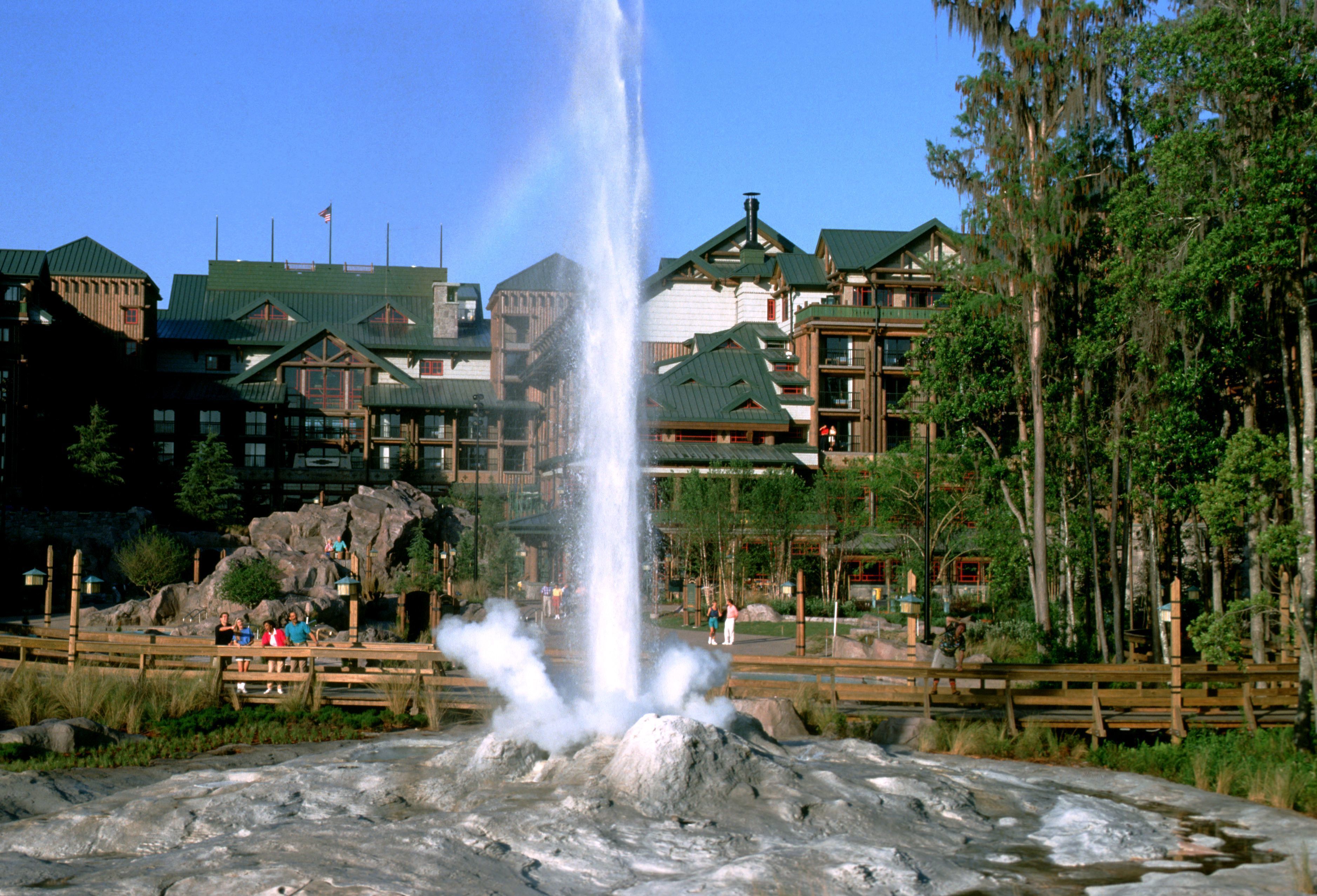 A hotel with a prominent water fountain in front, surrounded by lush greenery and a wooden deck.