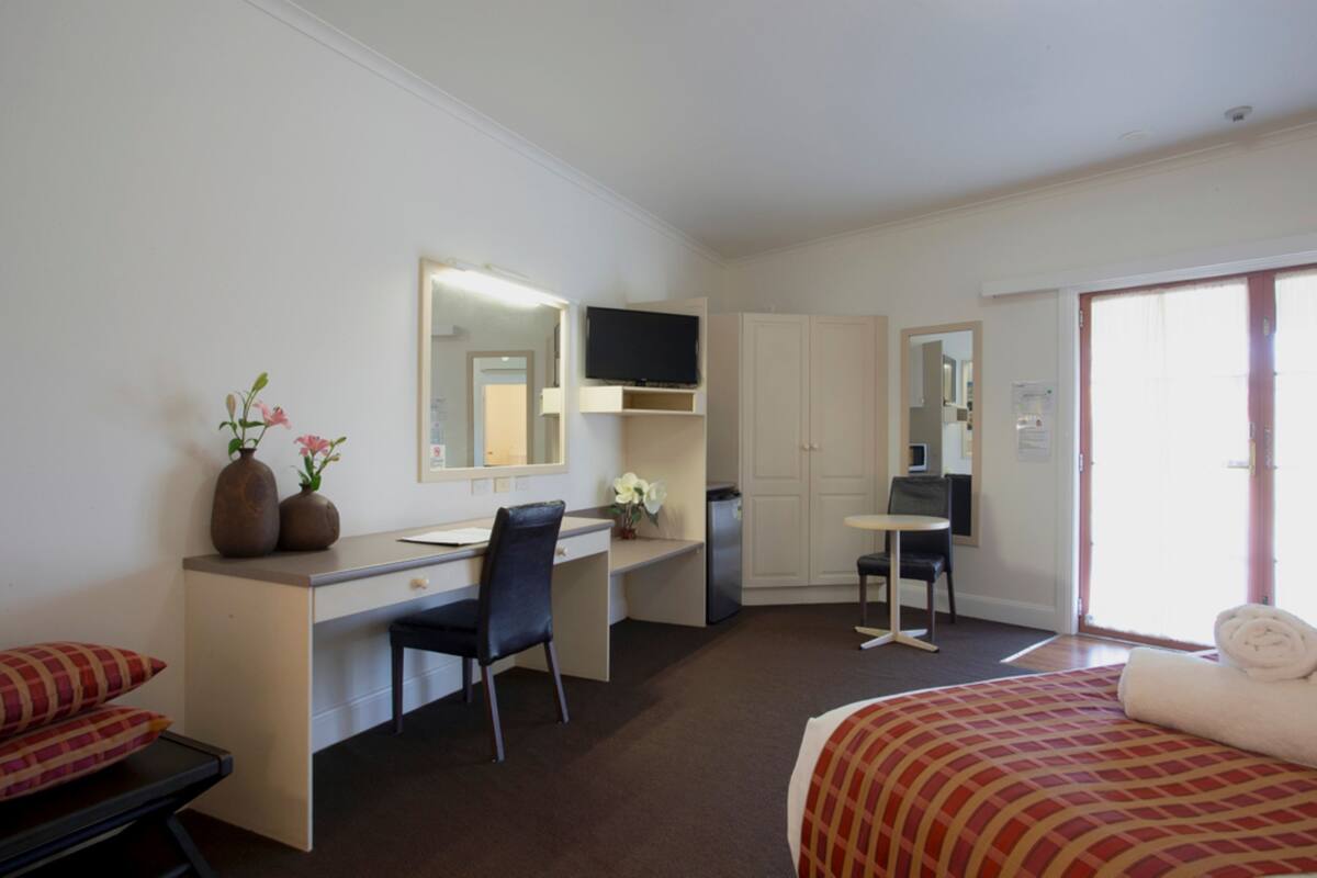 A hotel room with a bed, desk, chair, and a television.