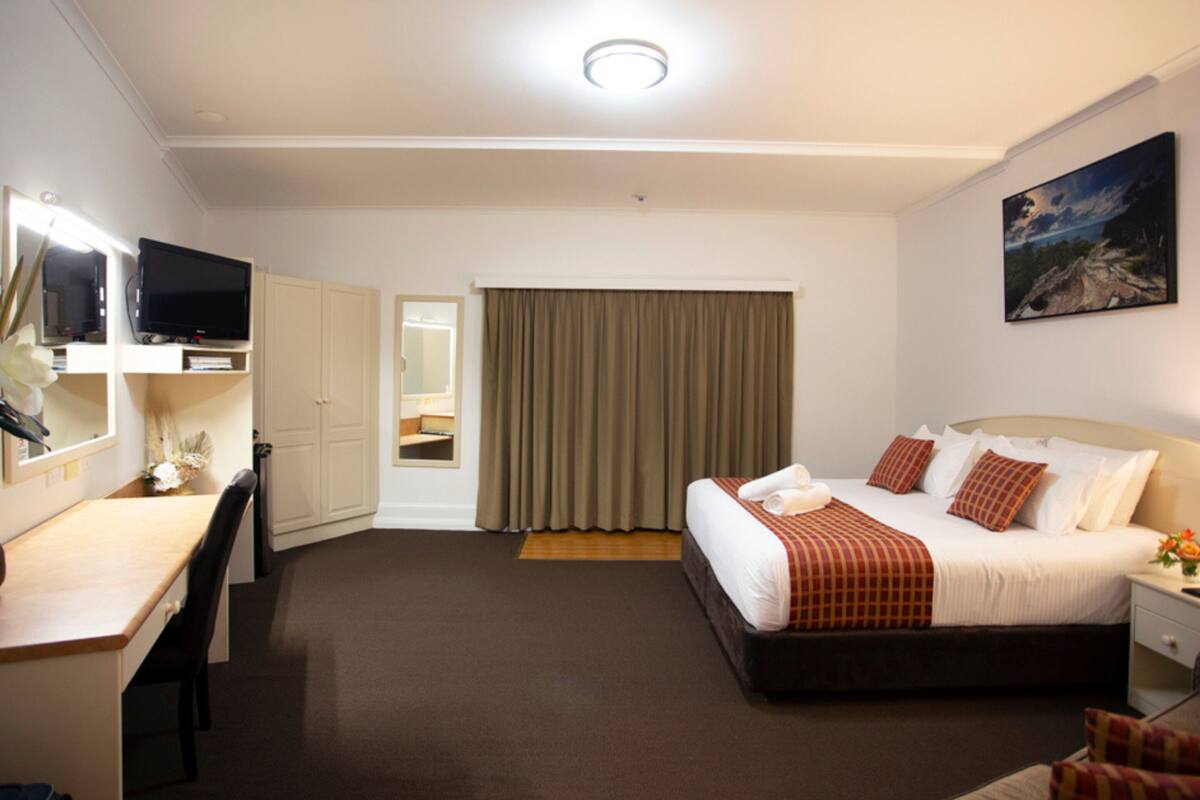 A hotel room with a bed, a desk, a television, a mirror, and a painting on the wall.