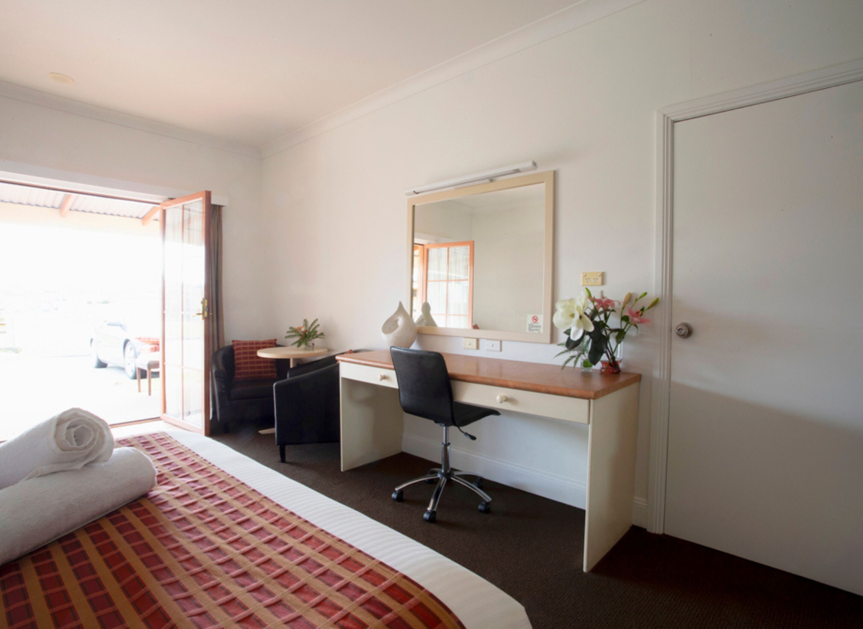 Hotelkamer met een bed, bureau, stoel, klein tafeltje, spiegel en een deur.