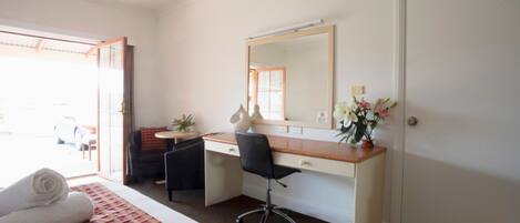 A hotel room with a bed, a desk, a chair, a small table, a mirror, and a door.