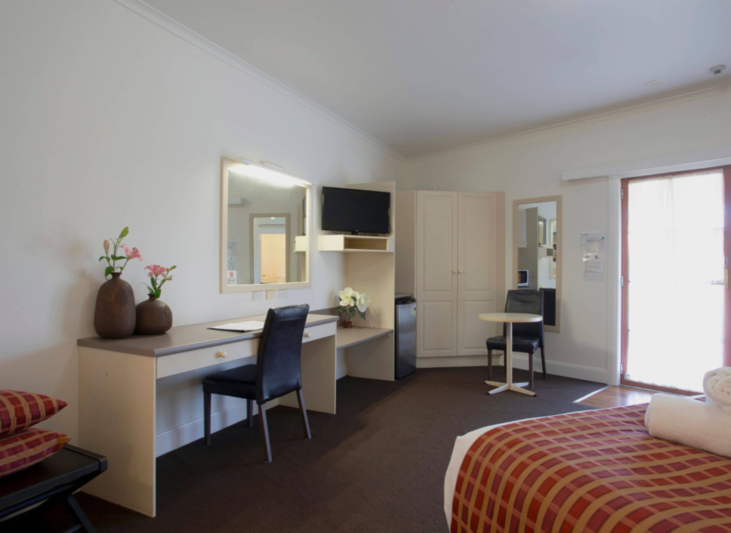 A hotel room with a bed, a desk, a chair, a television, and a wardrobe.