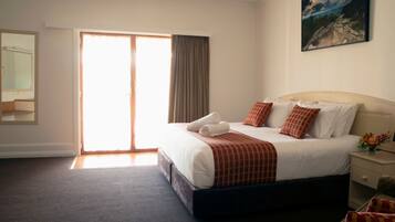 A hotel room with a large bed, a painting on the wall, a mirror, and a sliding door to the outside.