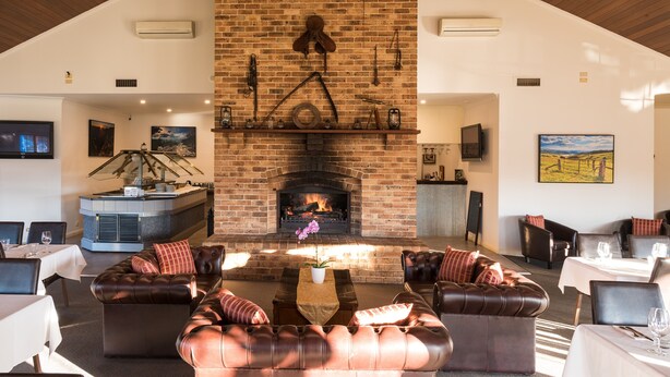 Un amplio salón con chimenea de ladrillo, sofás de cuero y una mesa de comedor preparada para cuatro personas.