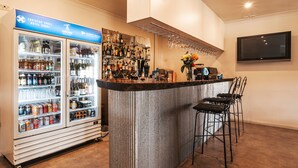 Una zona de bar con un refrigerador lleno de bebidas, una barra con diversas opciones para beber y un televisor montado en la pared.
