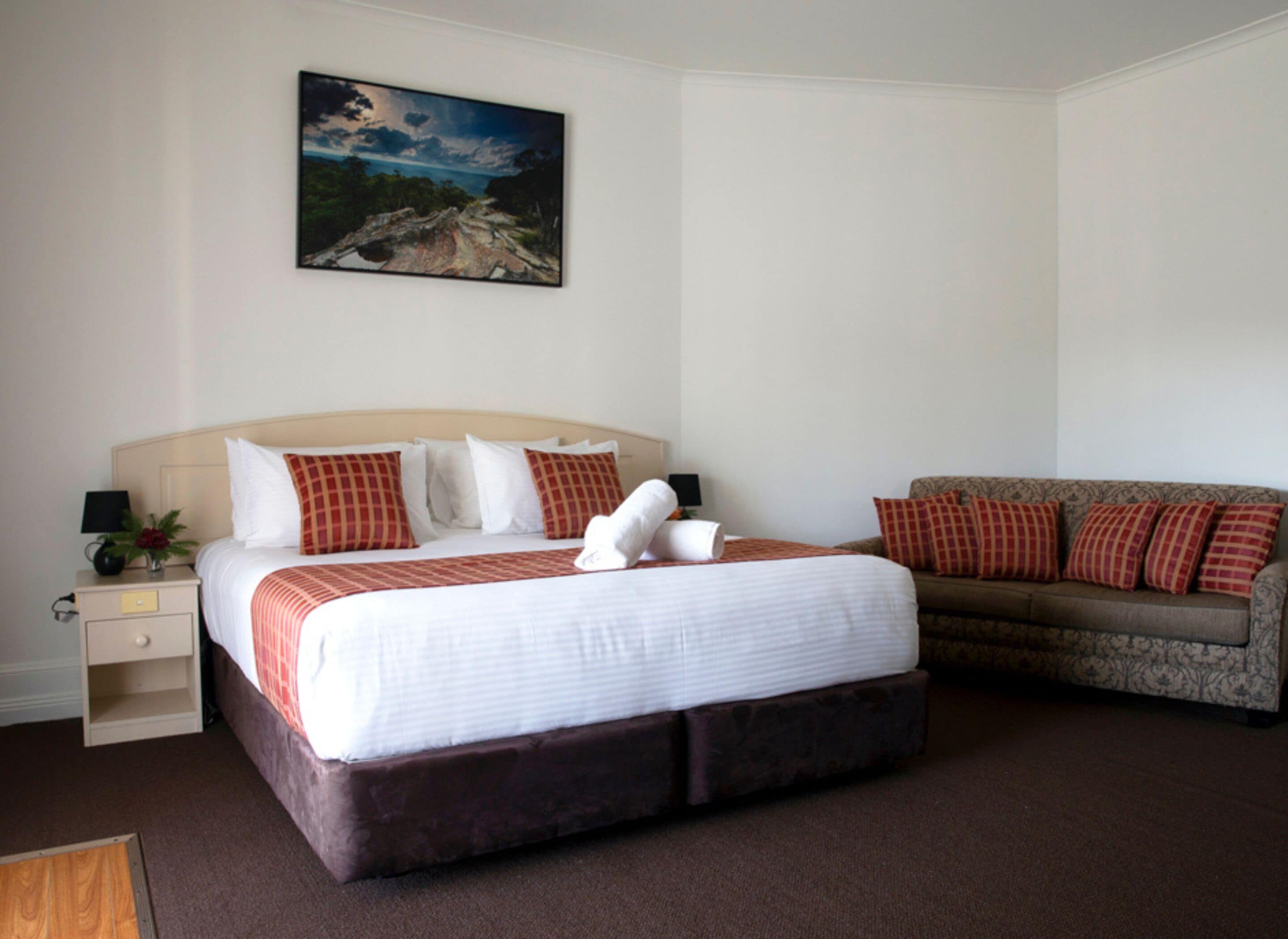 Una habitación de hotel con una cama grande, un sofá, una mesita de noche y un cuadro en la pared.