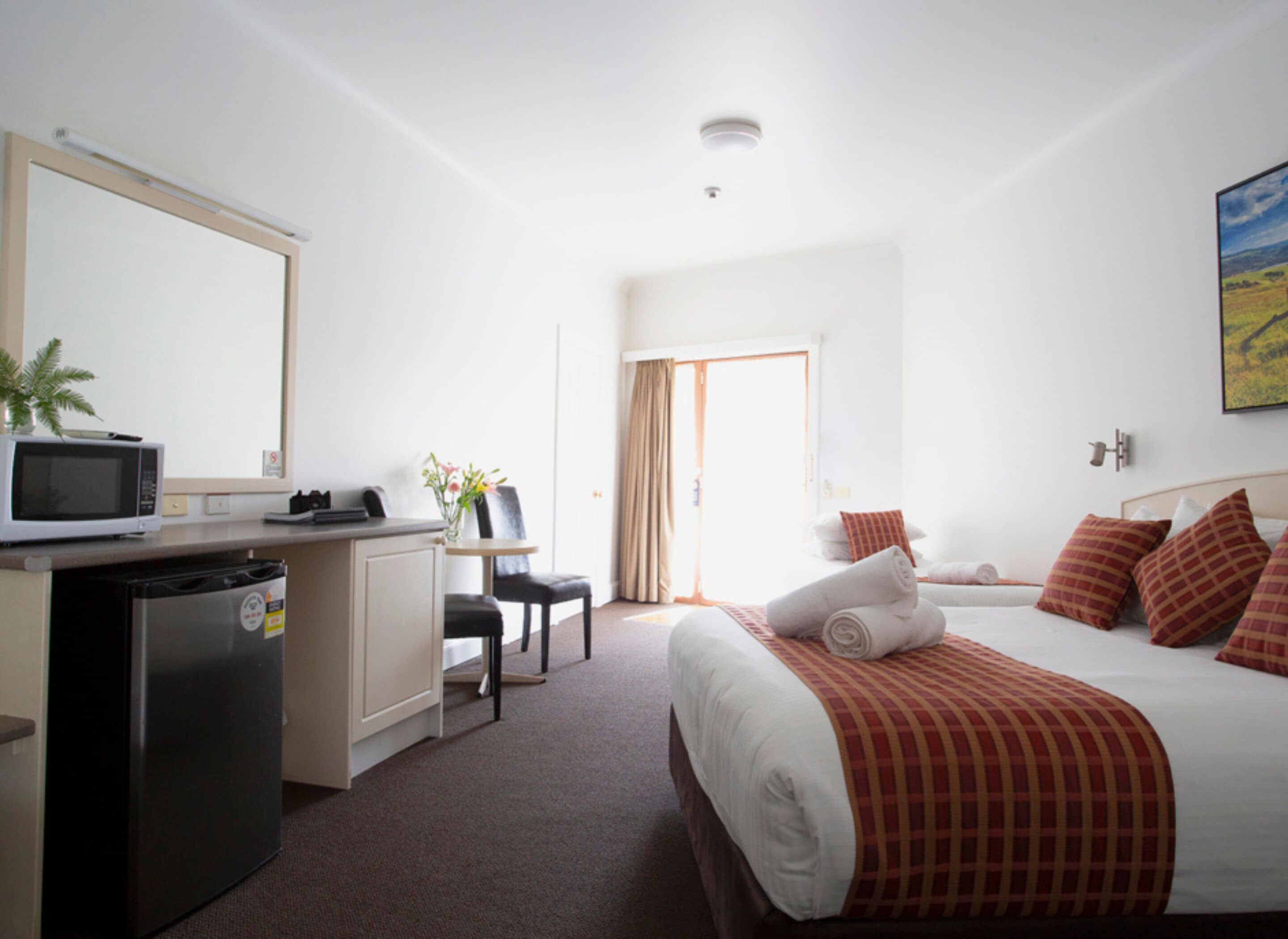 A hotel room with a bed, a desk with a computer, a microwave, and a small refrigerator.