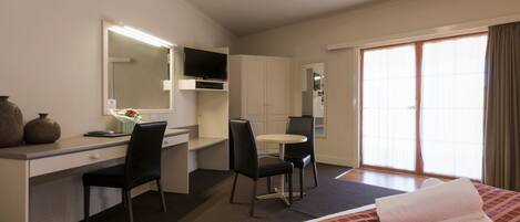 A hotel room with a bed, a desk with a chair, a television, and a sliding door to a balcony.