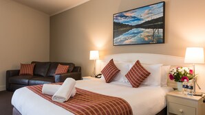 Una habitación de hotel con una cama, un sofá, una mesita de noche, una lámpara y un cuadro en la pared.