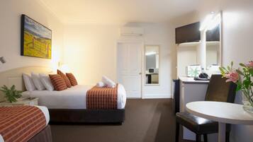 A hotel room with a bed, bedside table, lamp, and a desk with a chair.