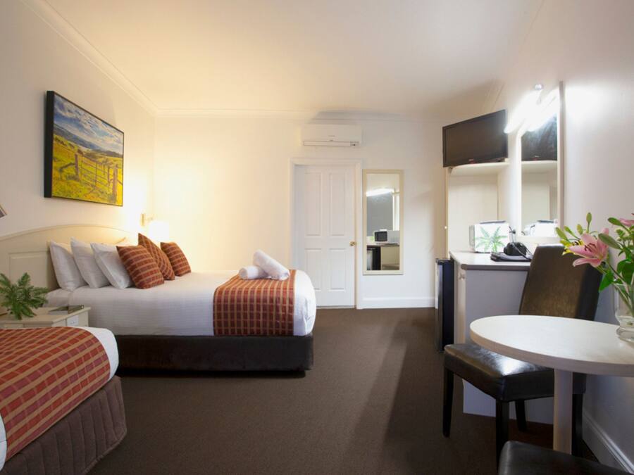 A hotel room with a bed, bedside table, lamp, and a desk with a chair.
