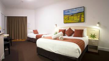A hotel room with two beds, a desk, a chair, a desk lamp, and a painting on the wall.