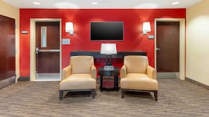 A hotel lobby with red walls, two leather armchairs, a flat-screen TV, and a small table with a lamp. - Extended Stay America Suites Sacramento Vacaville (Vacaville)