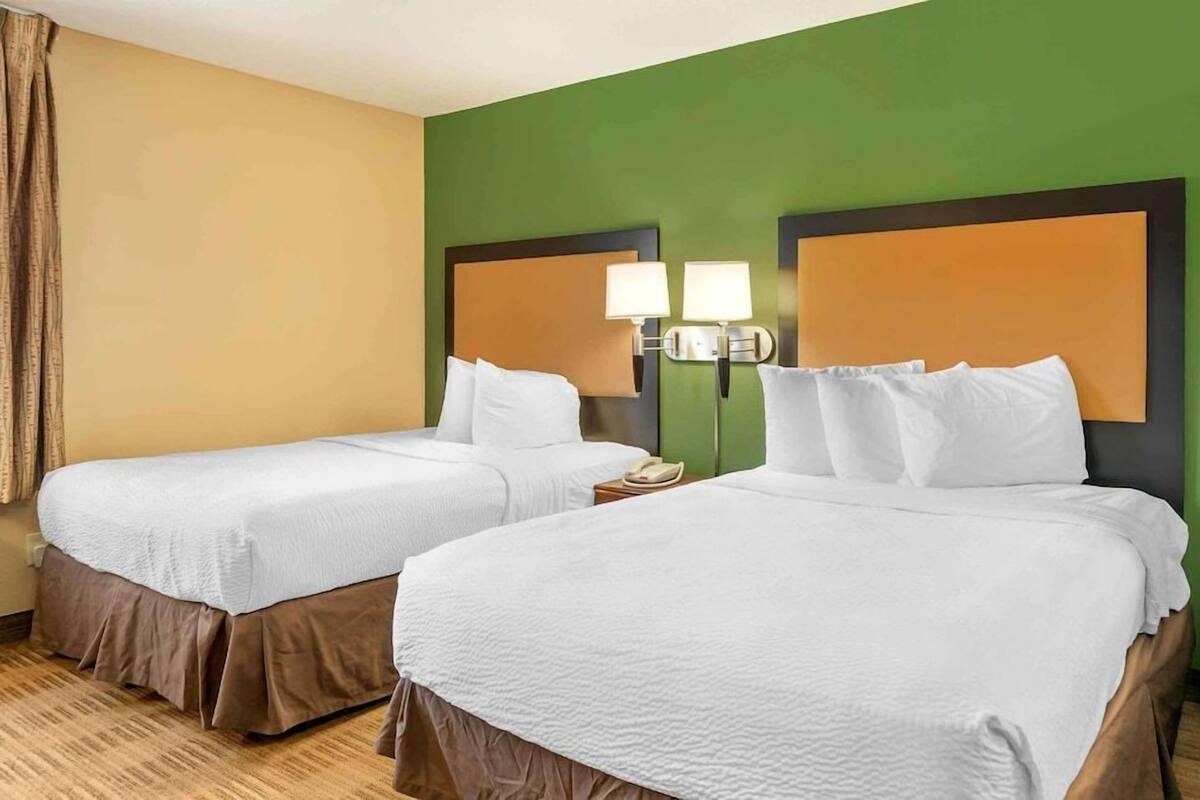 Une chambre d’hôtel avec deux lits, une table de chevet avec un téléphone et une lampe fixée au mur.