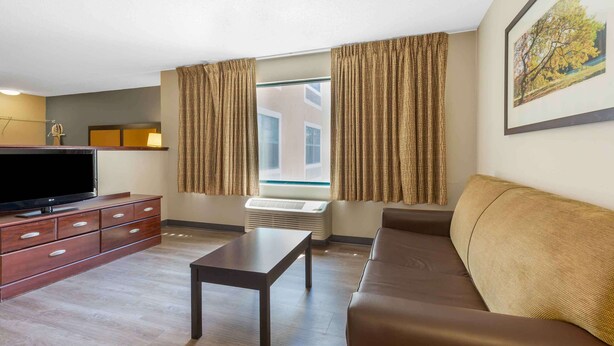 A modern living room with a flat-screen TV, a sofa, a coffee table, and a window with curtains. - Extended Stay America Suites Sacramento Vacaville (Vacaville)