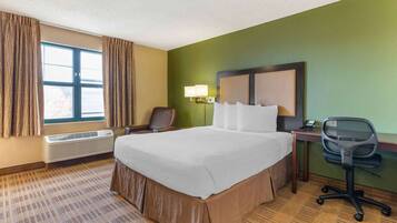 A hotel room with a large bed, a desk with a chair, a lamp, and a window with curtains.