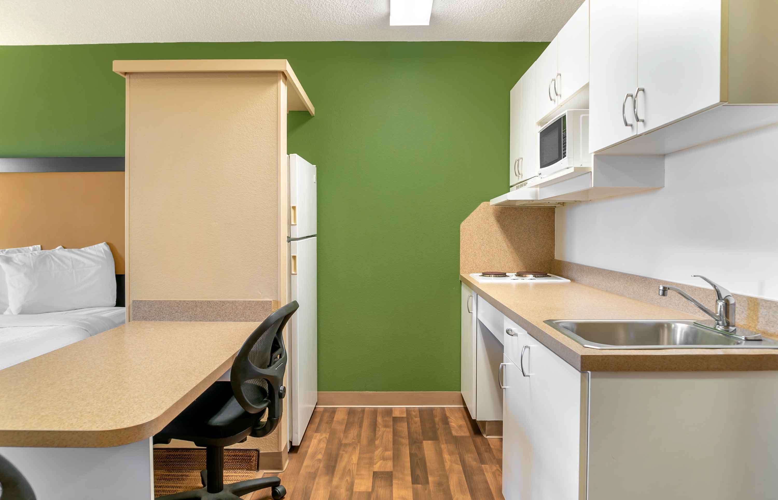 A compact room with a kitchenette, a bed, and a chair.