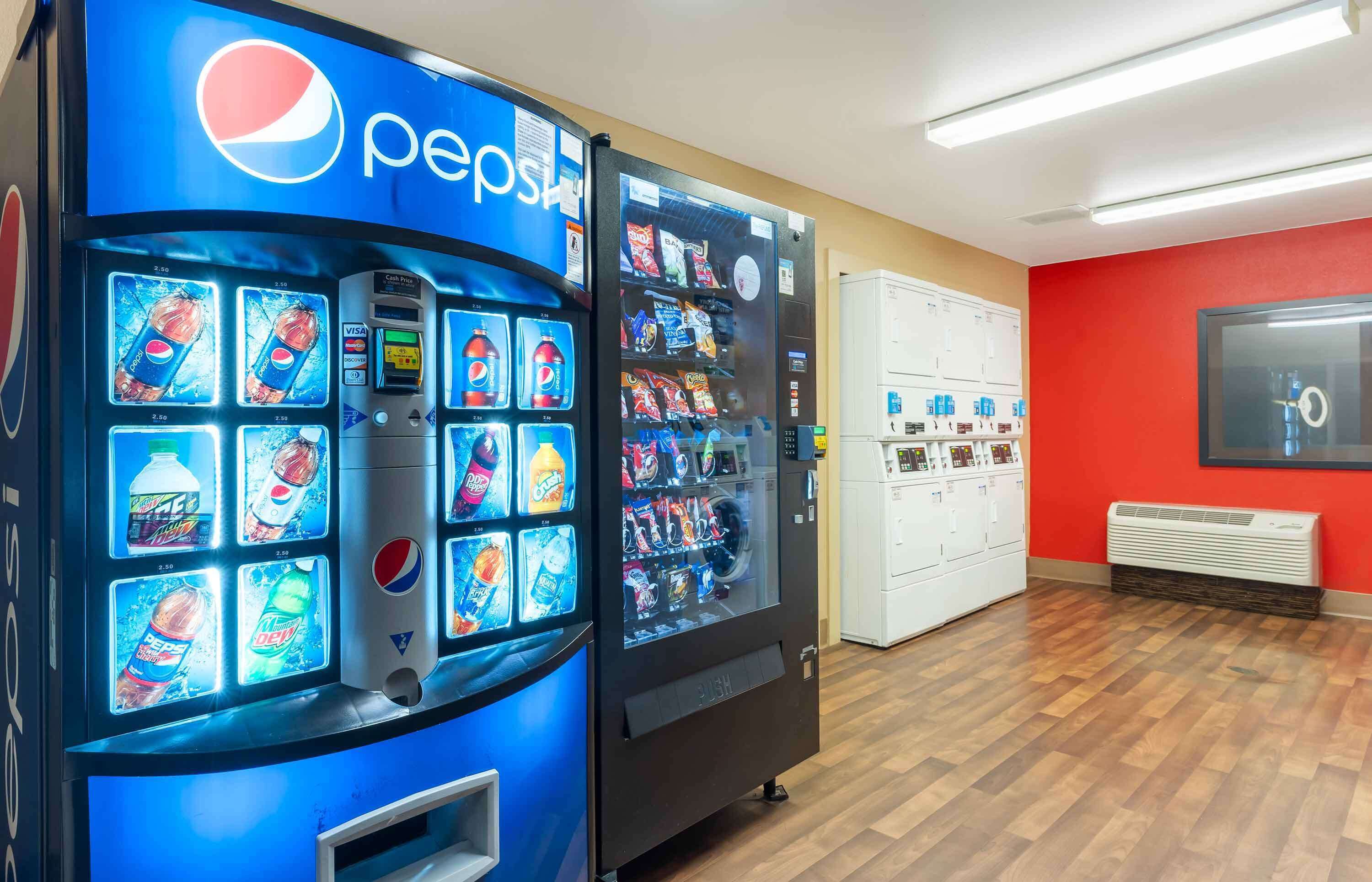 Un espace équipé de distributeurs automatiques proposant des produits Pepsi et d’autres boissons, un vestiaire blanc et un mur rouge.