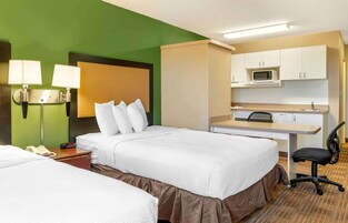 Una habitación de hotel con dos camas, un escritorio con una silla, un microondas y un teléfono en la mesita de noche.