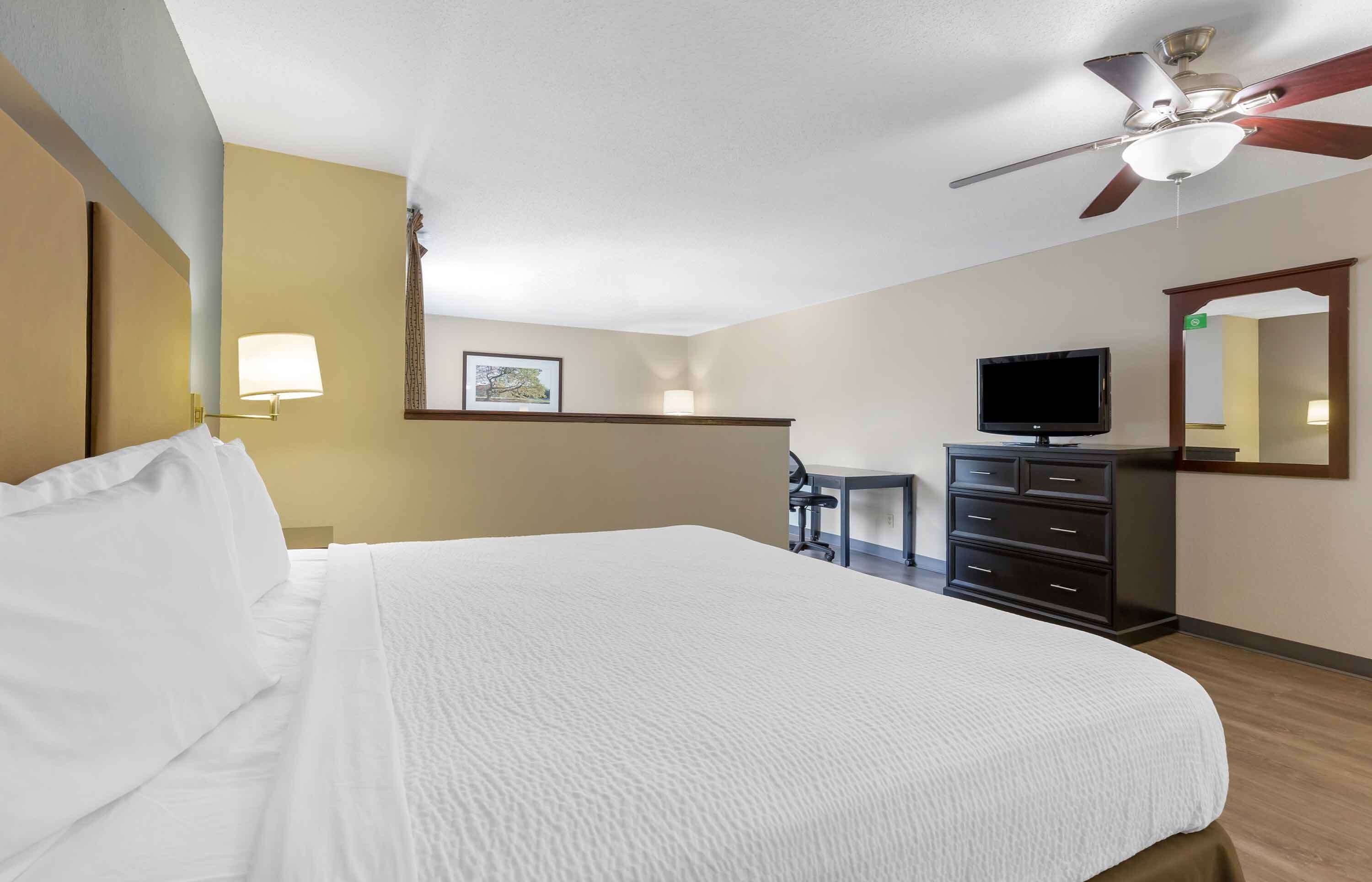 A hotel room with a large bed, a desk, a television, and a ceiling fan.