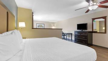 A hotel room with a large bed, a desk, a television, and a ceiling fan.