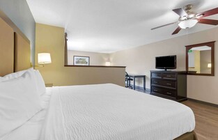 A hotel room with a large bed, a desk, a television, and a ceiling fan.