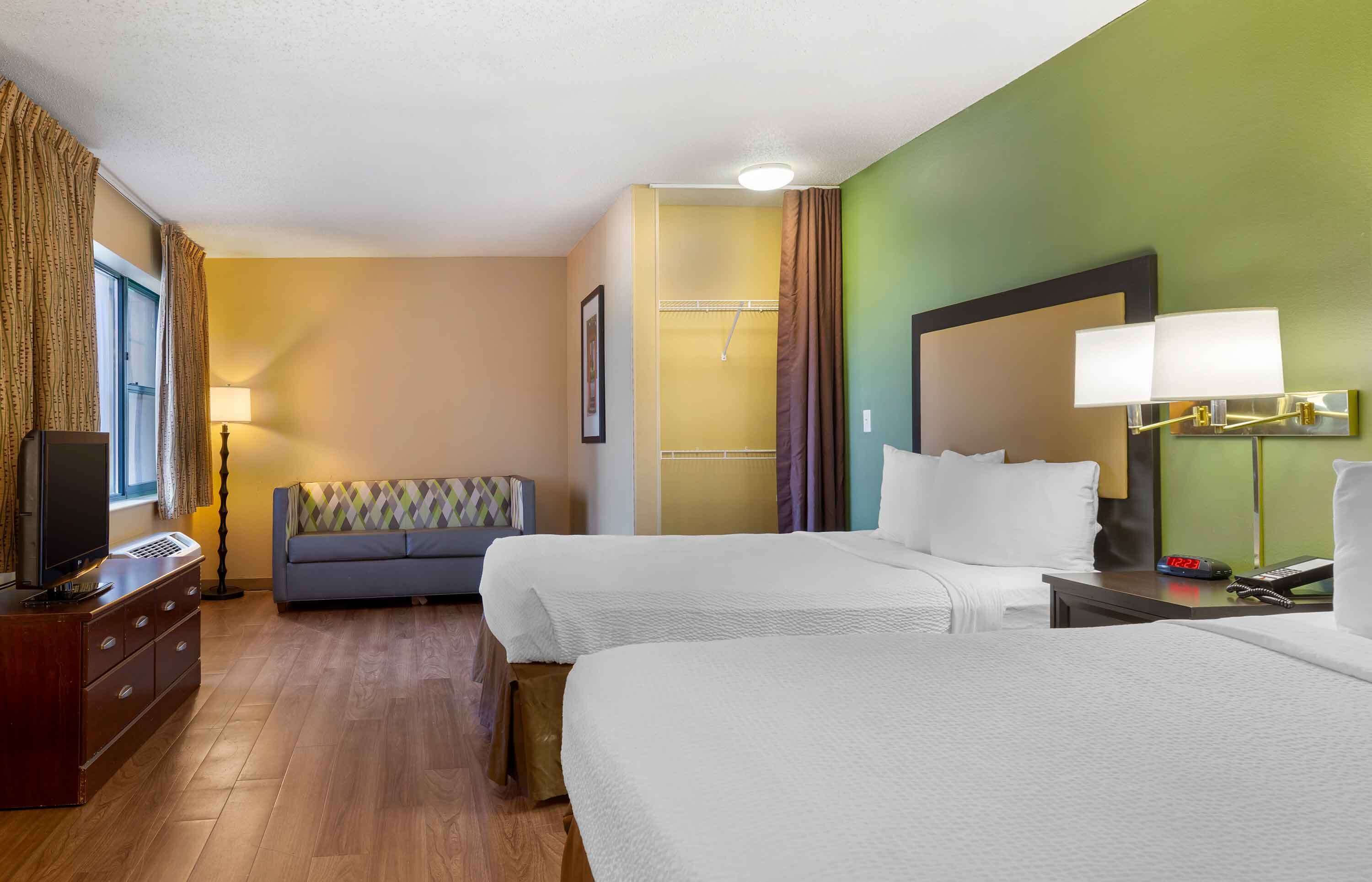A hotel room with two beds, a sofa, a TV, a dresser, and a lamp.