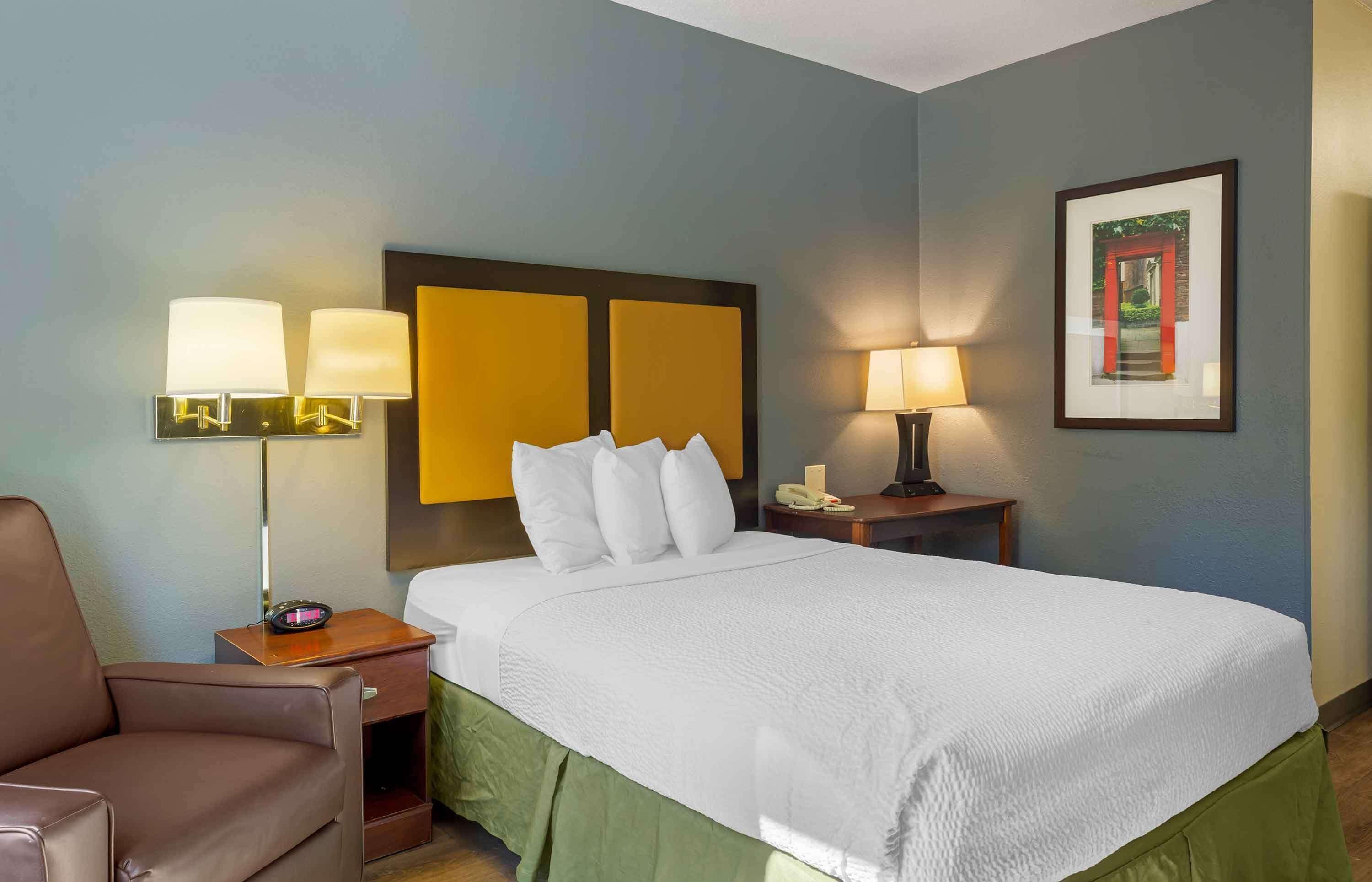 Une chambre d’hôtel avec un grand lit, deux tables de chevet avec des lampes, une chaise et un tableau encadré au mur.
