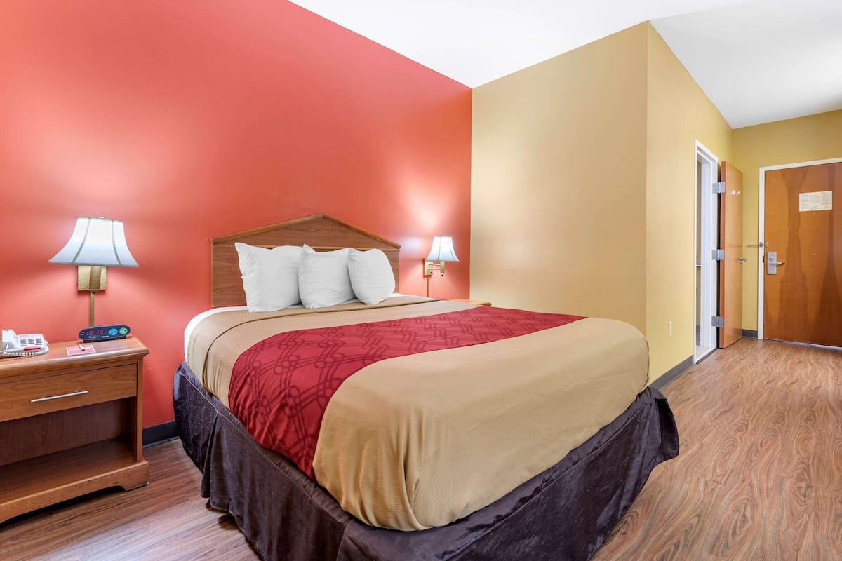Een hotelkamer met een bed, nachtlampjes, een nachtkastje en een houten vloer.