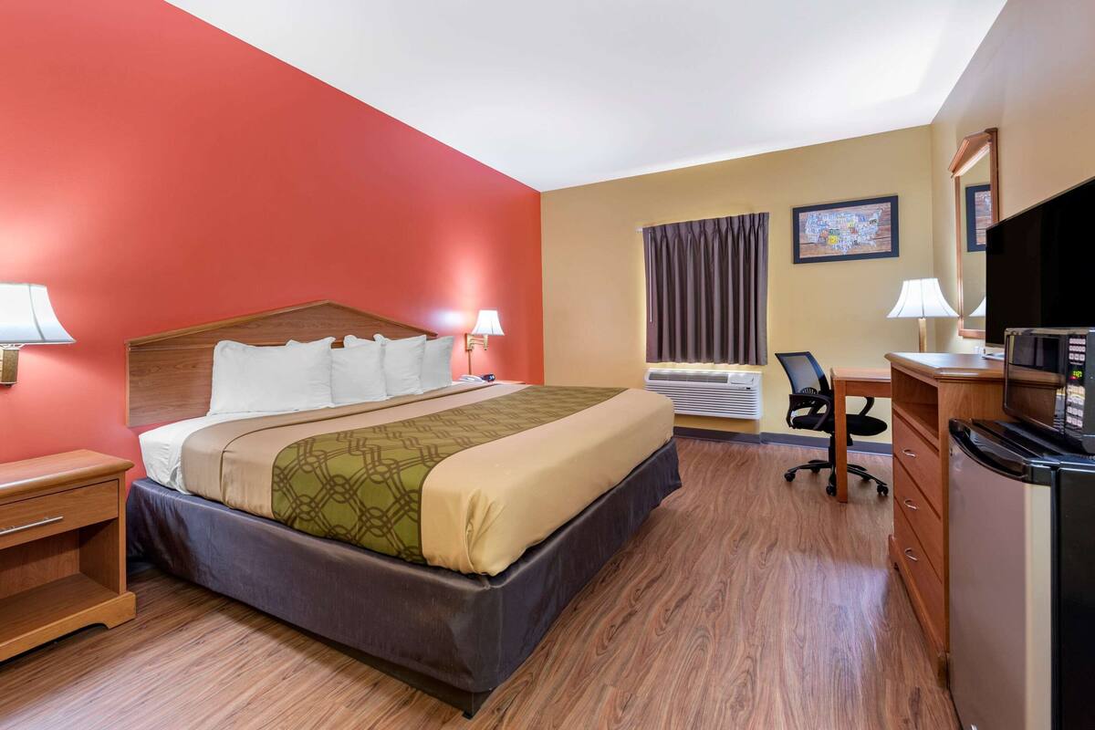 Een hotelkamer met een bed, nachtkastjes, een bureau met stoel, een televisie en een airconditioner.