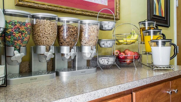 Een ontbijtbuffet met cornflakesdispensers, een fruitmand en een juskan.