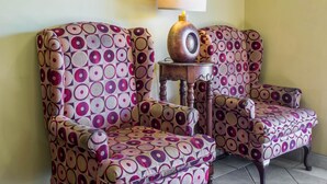 Een kamer met twee gestreept fauteuils, een houten bijzettafeltje met een lamp, en een spiegel aan de muur.