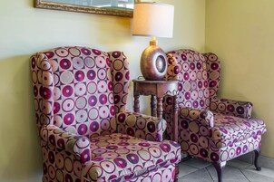 Una habitación con dos sillones estampados, una mesita de madera con una lámpara y un espejo en la pared.