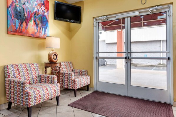 Un hall de hotel con dos sillones estampados, un televisor y un amplio ventanal que da al exterior.
