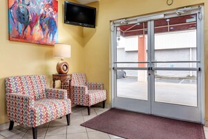 Un hall de hotel con dos sillones estampados, un televisor y un amplio ventanal que da al exterior.